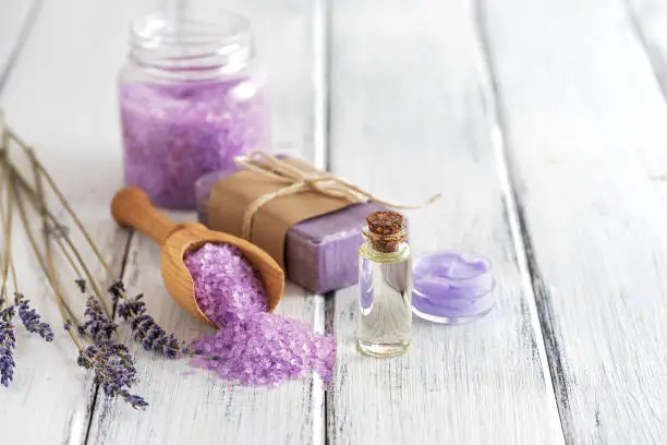 Lavender spa products on an old white wooden table. Body care products with lavender- oil, salt, cream, soap and dried lavender flowers. Selective focus.