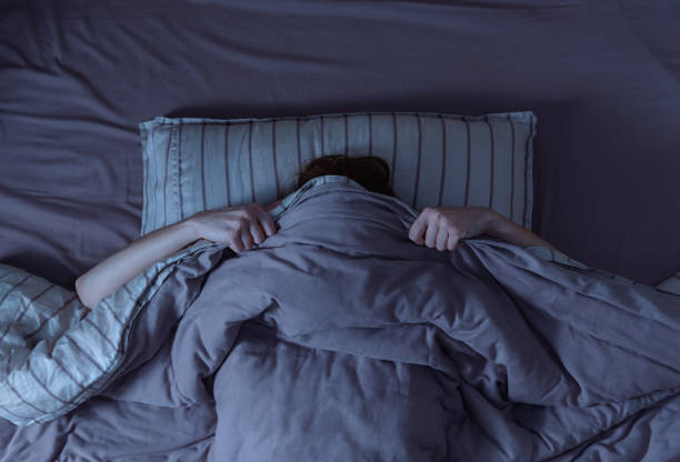 Scared woman in bed. Top view of scared woman in bed covering her face with blanket. woman sleeping in bed at night stock pictures, royalty-free photos & images