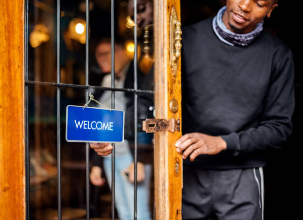 Cafe worker turning welcome sign board on front door after reopening of business post pandemic