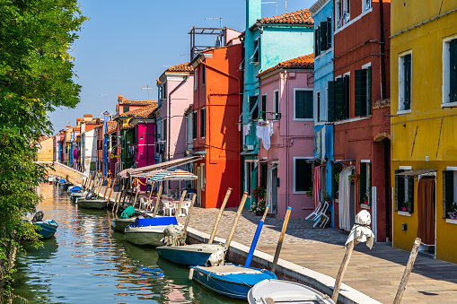 Boat, ancient walls, European architecture, rustic buildings, old city, water canals, waterways. Narrow canal in Venice, Italy sided by buildings with balconies and an old boat in the water.