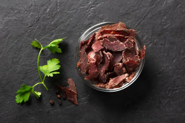 Bowl with jerky meat on a dark background, top view