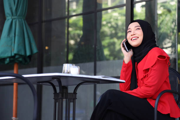 istock Muslim lady wearing hijab using mobile phone while drinking coffee at the local cafe in the city square 1305787587