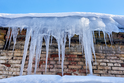 Many large icicles hang from the roof of an old brick building.