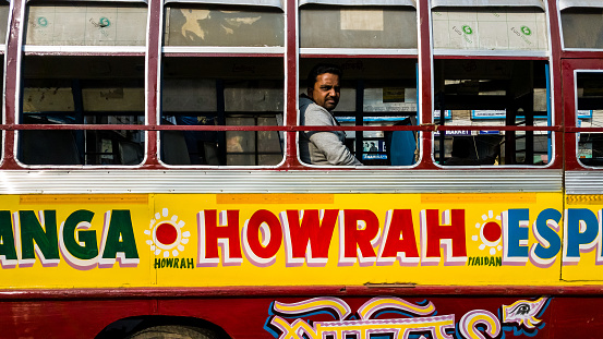 Kolkata, West Bengal, India - January 2018: An Indian male passenger sitting in a colorfully painted public transport bus in the city of Kolkata.