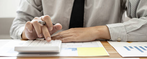 Close-up view A businessman using a calculator to calculate numbers on a company's financial documents, he is analyzing historical financial data to plan how to grow the company. Financial concept. vista de primer plano un hombre de negocios que usa una calculadora para calcular números en los documentos financieros de una empresa, está analizando datos financieros históricos para planificar cómo hacer crecer la compañía. concepto financiero.