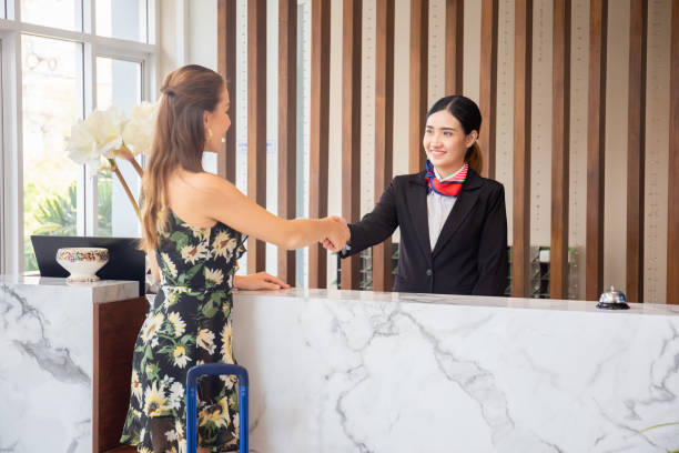 istock Happy receptionist and guest making handshake at hotel reception, receptionist standing at hotel counter with young female travellers 1305793228