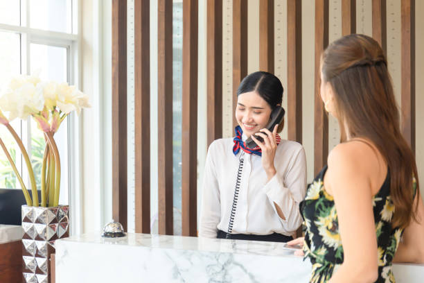 Young woman receptionist talking on the phone at workplace with female travellers standing at reception desk in hotel Young woman receptionist talking on the phone at workplace with female travellers standing at reception desk in hotel hotel reception hotel business lobby stock pictures, royalty-free photos & images