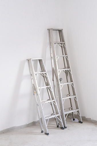 two aluminium stairs ladder lean on white cement wall. high and tall abstract image in construction new house.