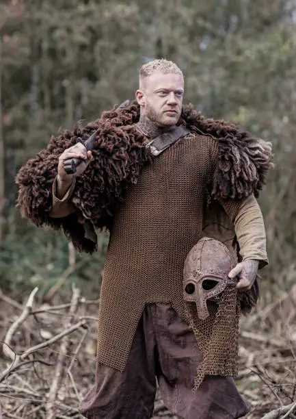A handsome blonde viking warrior soldier holding a weapon in a wintry forest
