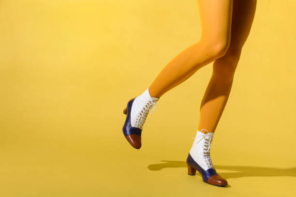 Woman wearing mustard-colored pantyhose and retro tritone shoes Woman wearing mustard-colored pantyhose and retro tritone shoes or ankle boots with laces in a close up side view with leg raised over a yellow background with copyspace lace up stock pictures, royalty-free photos & images