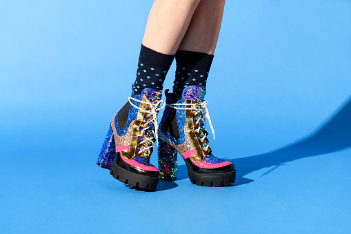 Trendy woman wearing ankle boots with laces decorated with sparkling sequins and gold trim in a close up on her lower legs over a blue background with copyspace