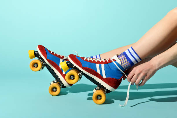 Young woman tying the laces on her red and blue rollerskates Young woman tying the laces on her red and blue rollerskates with colorful yellow wheels in a close up side view of her feet and hands over a blue background with copyspace lace fastener photos stock pictures, royalty-free photos & images
