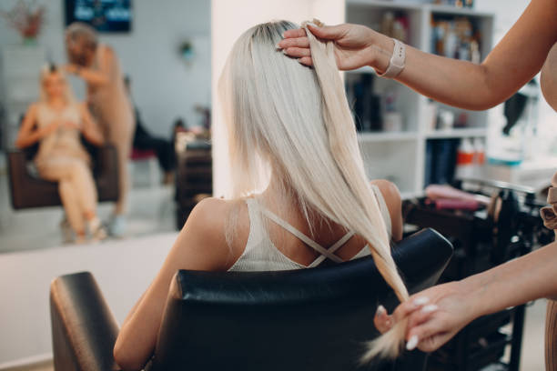 Hairdresser female making hair extensions to young woman with blonde hair in beauty salon. Professional hair extension. stock photo