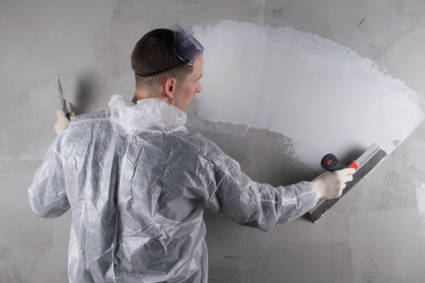 istock master in a protective suit is working on leveling the concrete wall with a large spatula, applying a white solution, there is a place for the inscription, rear view 1305811244
