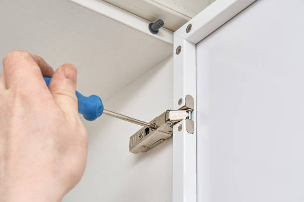 istock Man adjusts furniture hinge with screwdriver installing case 1305816063