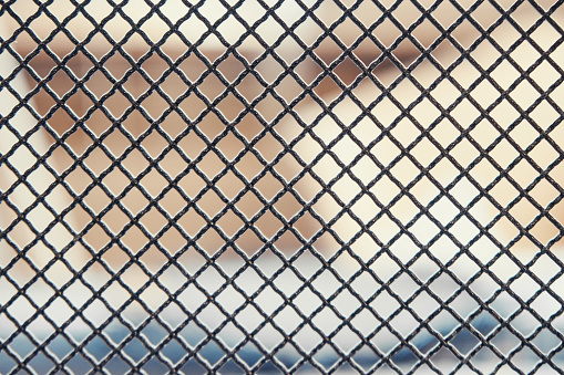 Dark metal fence grid with pattern of numerous small shaped cells installed on light blurred background extreme close view