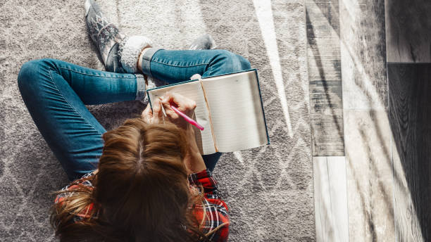 Woman writing into her diary. Young woman sitting on the floor at living room and writing into her diary note pad stock pictures, royalty-free photos & images