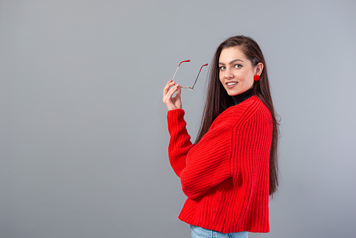 young emotional teenage woman with glasses dressed in a red sweater posing on a gray background