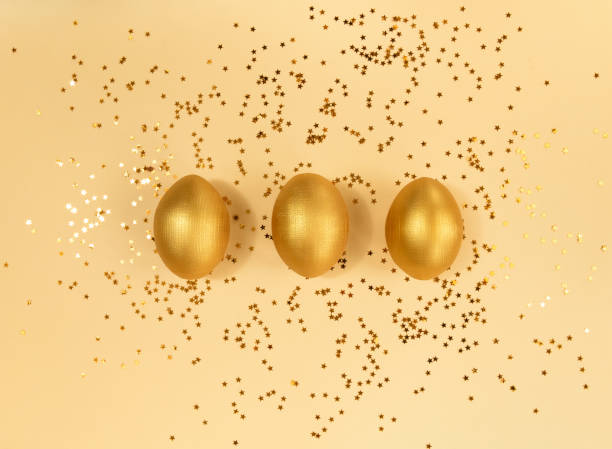 istock Three easter wooden golden eggs and confetti on beige backdrop. 1305822805