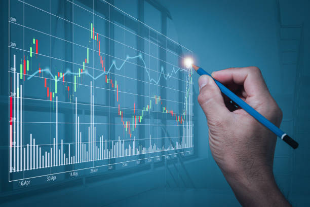 istock A man's hand holding a pencil makes a gesture written on a stock chart that is making new highs. A blurry backdrop of the office's large windows on high-rise buildings. 1305822847