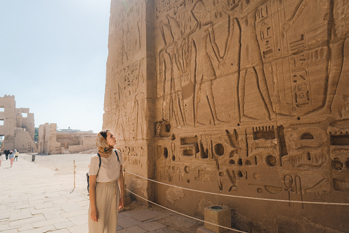 A happy tourist girl interested in Egyptology and archaeology and gets a travel experience at the Karnak Temple in Luxor among alley of sphinxes in Thebes