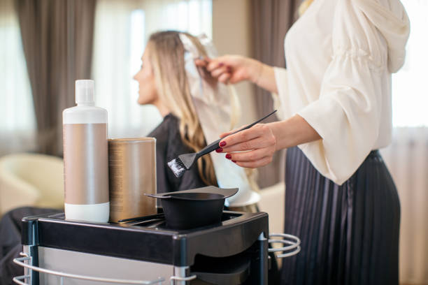 Woman dyeing her hair at the salon Blonde woman dyeing her hair at the salon. She is sitting and the hairdresser/hairstylist is putting hair color on her hair. This is regular hair care treatment in customers favorite salon. dye stock pictures, royalty-free photos & images