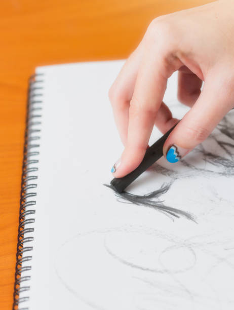 istock Young woman's hand sketches in a spiral notebook with a charcoal pencil 1305825773