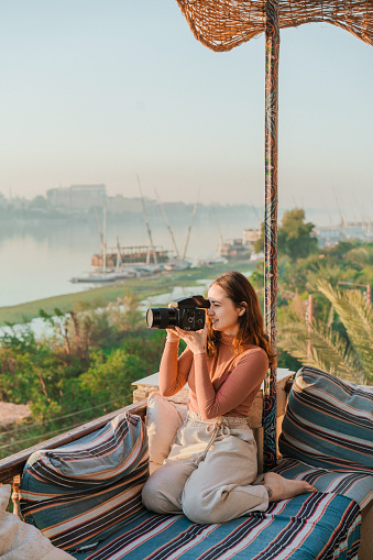 Young Caucasian woman sitting on terrace and  photographer Nile at sunset in Luxor