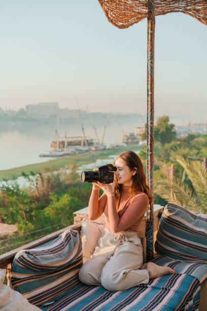 Woman sitting on terrace and  photographer Nile at sunset in Luxor Young Caucasian woman sitting on terrace and  photographer Nile at sunset in Luxor luxor thebes stock pictures, royalty-free photos & images