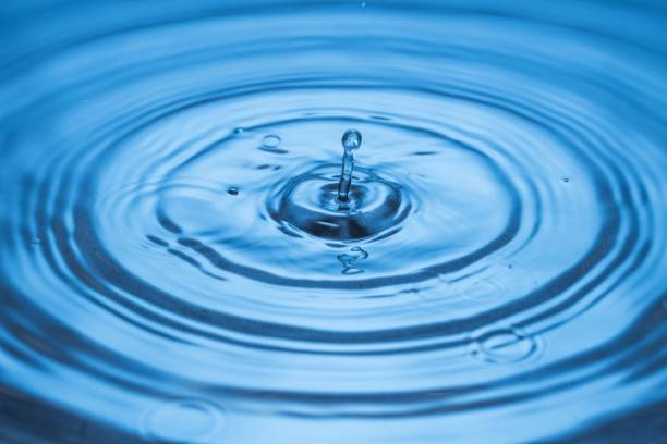 istock Close up view of Drops making circles on blue water surface isolated on background. 1305826247