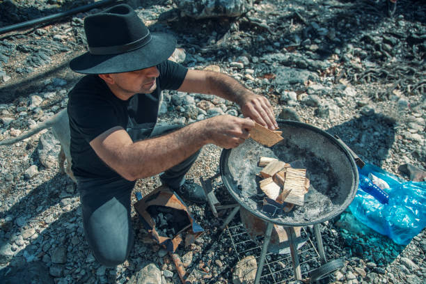 istock Man in cowboy hat is preparing fire for barbecue at picnic. 1305826979