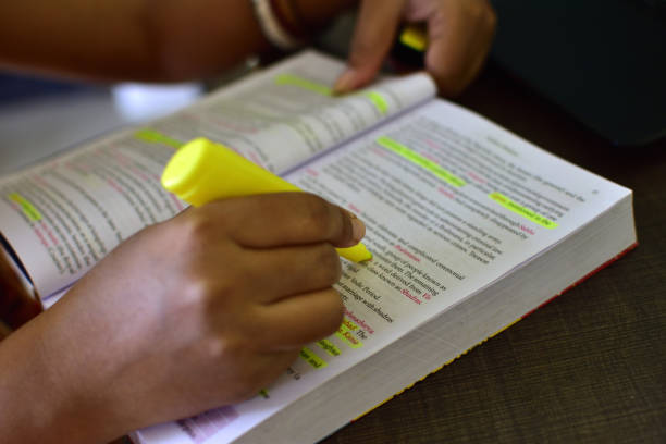 Closeup view of a woman using a highlighter while studying inside the home.