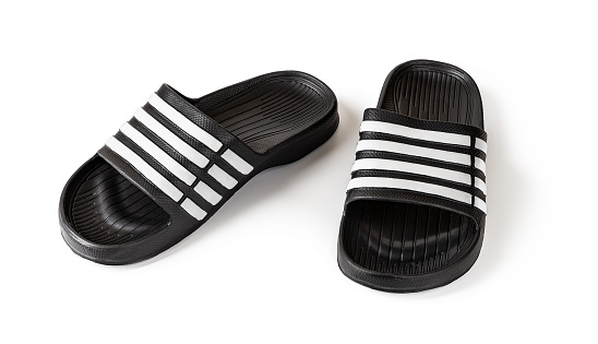 Pair of slide sandals isolated on white. Black rubber slippers closeup. Light shoes for pool or shower. Comfortable beach flip flops for hot weather and summer vacation. Front view.