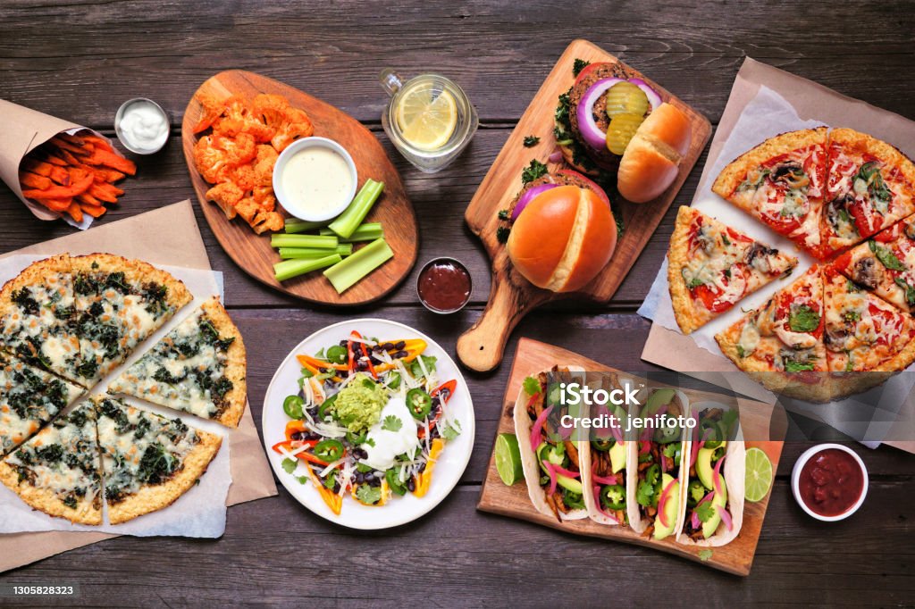Healthy plant based fast food table scene. Top down view on a wood background. Healthy plant based fast food table scene. Top down view on a wood background. Cauliflower crust pizzas, bean burgers, mushroom tacos, bell pepper nachos and cauliflower wings and sweet potato fries. Pizza Stock Photo