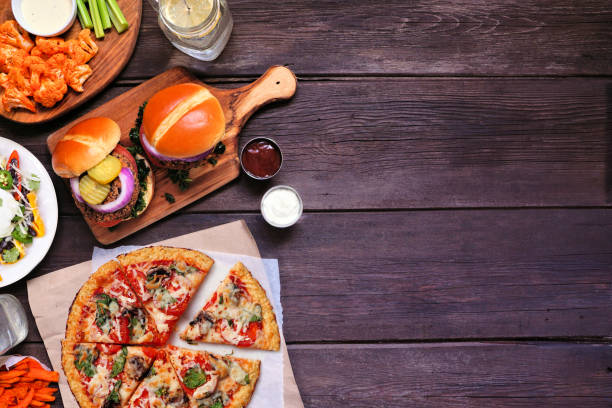 Healthy plant based fast food side border. Above view over a dark wood background. Copy space. Healthy plant based fast food side border. Above view over a dark wood background. Table scene with cauliflower crust pizza, bean burgers and vegetarian sides. Copy space. veggie burger photos stock pictures, royalty-free photos & images
