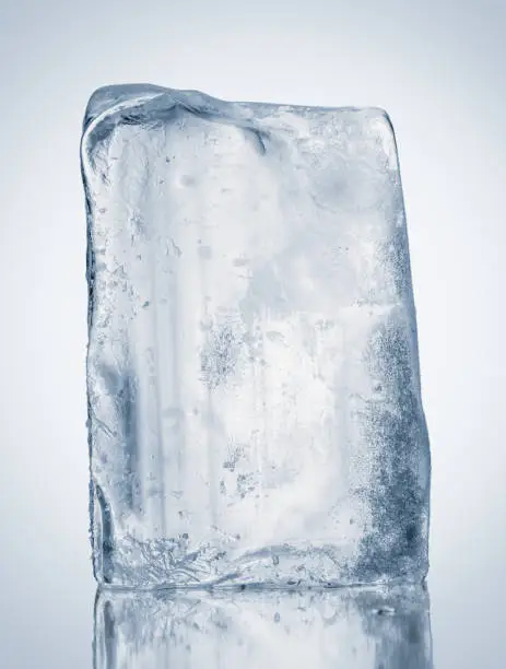 Crystal clear natural ice block in cold tones on a reflective surface. Clipping path included.