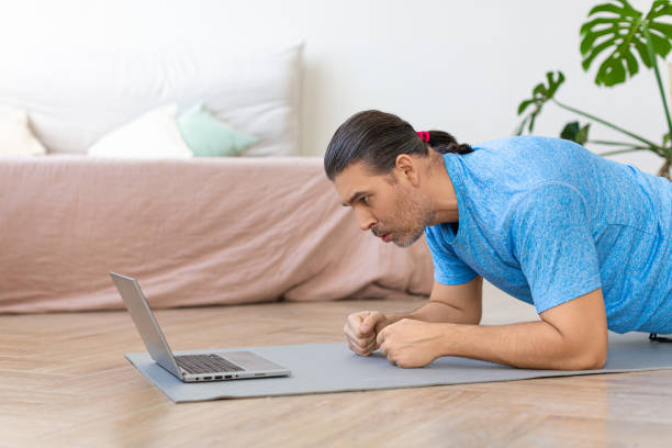 istock Photo of a middle-aged man doing the plank exercise. He follows the online tutorial from internet 1305831580