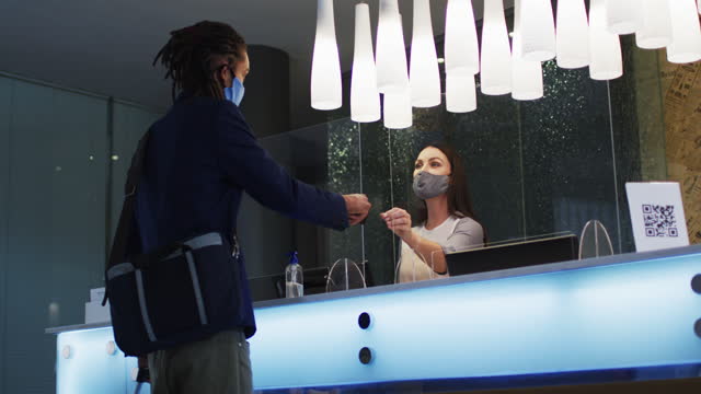 Mixed race man and female receptionist wearing face masks at hotel reception desk