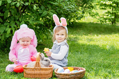 Happy Easter. Laughing child at Easter egg hunt with pet bunny. Little toddler girl playing with animal in garden. Cute funny girl with Easter eggs and bunny ears at garden.