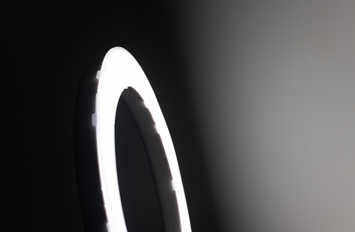 Large LED ring light in a studio room against empty walls side view and the very dark to bright light gradient wall effect.