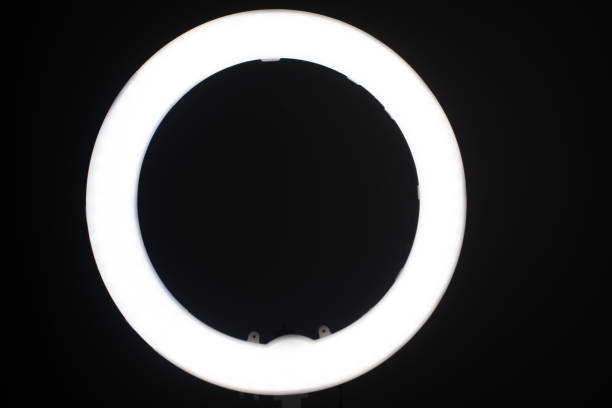 istock Large LED ring light in a studio room against empty walls front view and the very dark back walls. 1305835173