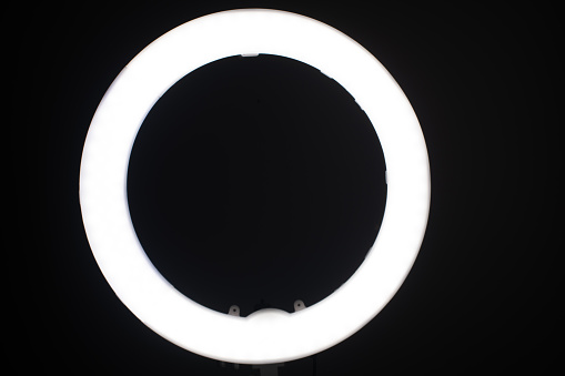 Large LED ring light in a studio room against empty walls front view and the very dark back walls.