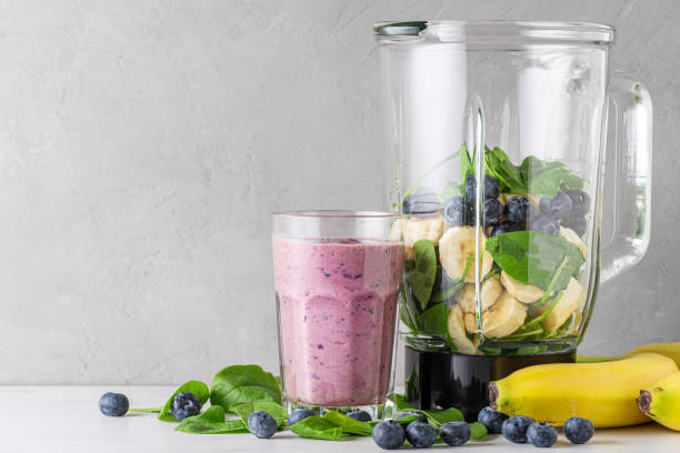 Glass of blueberry, banana and spinach smoothie with fresh juicy ingredients in blender for making healthy drink Glass of blueberry, banana and spinach smoothie with fresh juicy ingredients in blender for making healthy drink. Vegan drink blender photos stock pictures, royalty-free photos & images