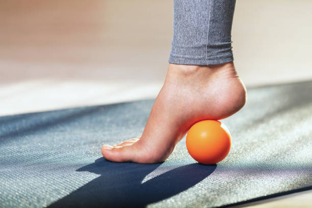 Myofascial release of hyper-movable muscles of the foot with a massage ball on a gymnastic mat at home. Prevention of leg fatigue after wearing high heel shoes stock photo