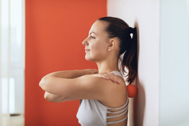 belle femme effectue la libération myofascial des muscles hyper-flexibles du dos avec une boule de massage près du mur. le concept de prévention de la fatigue du dos et d’auto-massage - massage ball photos et images de collection