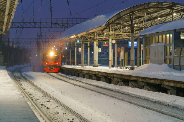 Electric train arriving at the blizzard Ramenskoe, Russia - February 14, 2021: Electric train coming at the station in the blizzard. Snowy sunset. Blue colors. Traveling concept. People standing on the platform and waiting for the train electric train photos stock pictures, royalty-free photos & images
