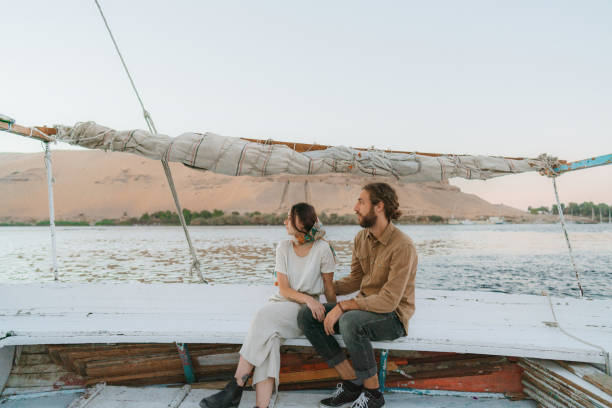 Young heterosexual couple traveling on felucca on the Nile at sunset Young Caucasian heterosexual couple traveling on felucca on the Nile at sunset felucca boat stock pictures, royalty-free photos & images