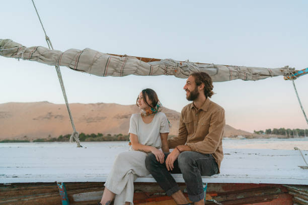 joven pareja heterosexual viajando en felucca en el nilo al atardecer - felucca boat fotografías e imágenes de stock