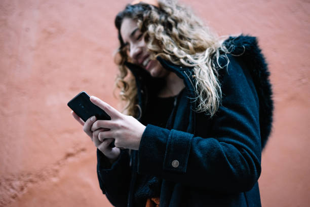 istock Young blonde woman sending a message with her cell phone on an orange wall while laughing. 1305842112