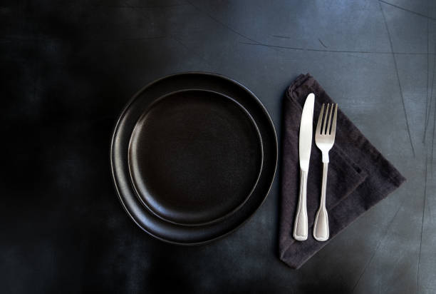 istock Black plate, cutlery and napkin on dark table 1305849063